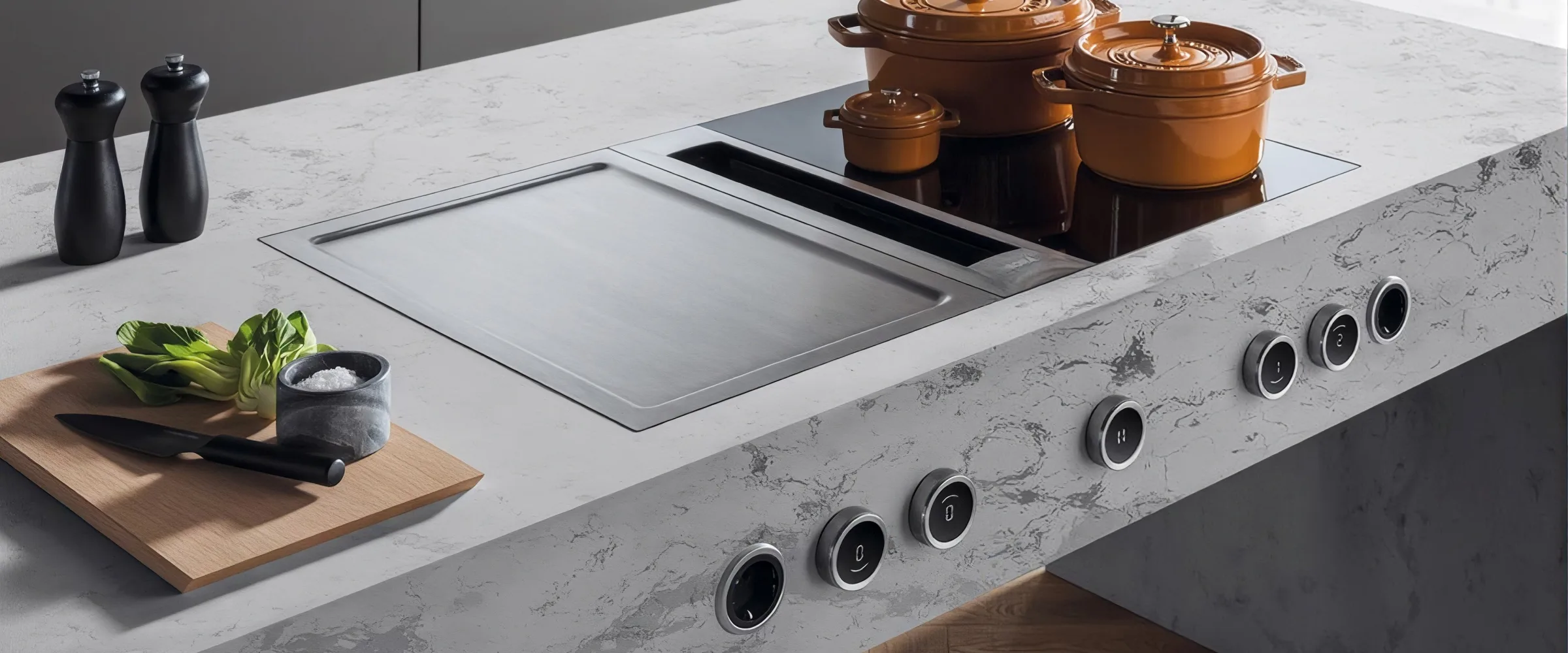 Modern kitchen countertop with integrated induction hob featuring multiple touch controls, copper cooking pots, marble worktop, wooden chopping board with fresh vegetables, salt and pepper mills, and a minimalist design aesthetic.