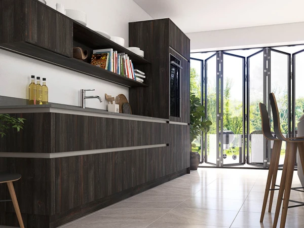 Modern kitchen with dark wood cabinetry and open shelving displaying books and kitchenware, leading to bi-fold glass doors opening onto a garden view, with wooden bar stools at the counter and white walls and tiled flooring.