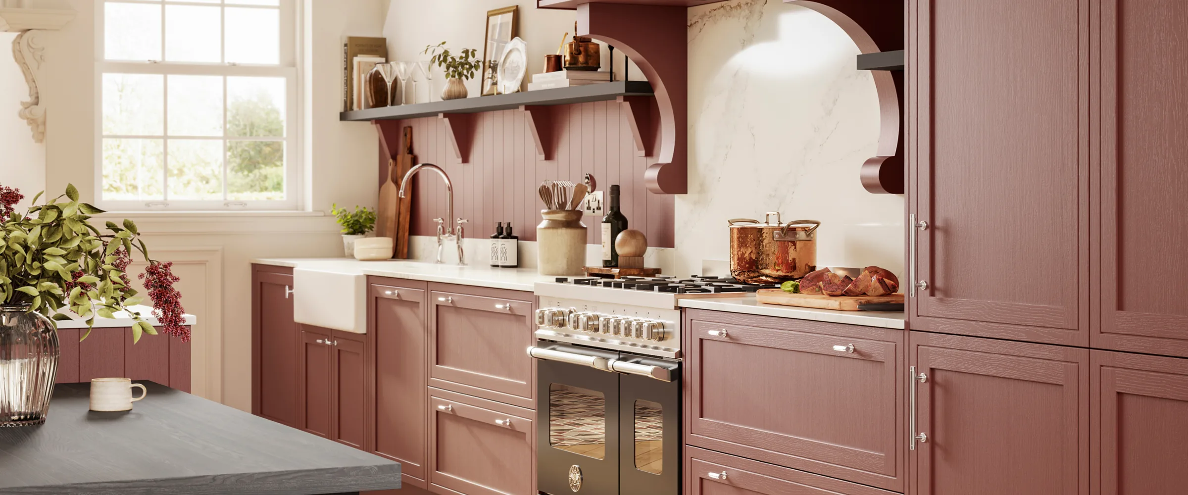 Modern kitchen with mauve-pink cabinetry, white farmhouse sink, cream-coloured Aga-style cooker, open shelving with decorative items, large windows with natural light, potted plants, and cream and burgundy colour scheme throughout