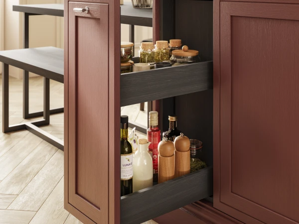 Kitchen island with burgundy wooden cabinetry and dark wood drawers displaying cooking ingredients, oils, spices and jars, positioned in a modern kitchen with dining table and window in background