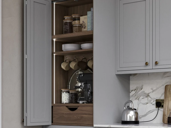 Open grey kitchen cabinet with illuminated shelves displaying storage jars, white plates, hanging cookware, coffee machine and kitchen accessories, with a silver kettle on the marble countertop below
