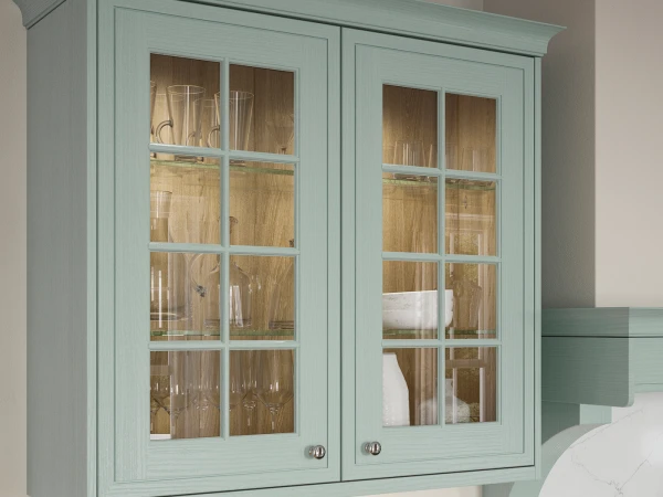 Light sage green wall-mounted cabinet with two doors featuring eight-pane glass panels, displaying glassware and white items on wooden shelves inside