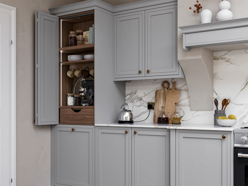 Modern kitchen with grey cabinetry featuring an open corner cabinet displaying wooden shelves with cookware, dishware and kitchen items, marble backsplash, white countertops, brass hardware, white floating shelves with decorative vases and dried flowers, and a silver kettle on the countertop