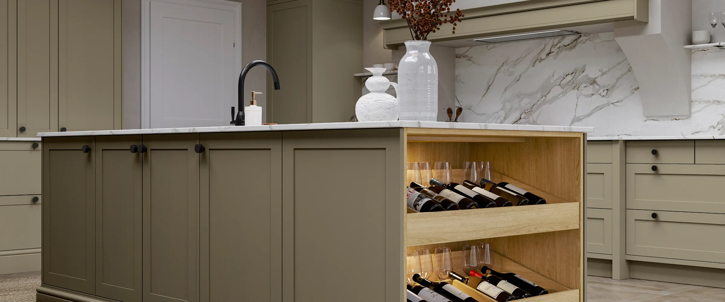 Modern kitchen with sage green cabinetry, white marble countertops and backsplash, an island featuring open wine storage with bottles displayed on wooden shelves, white ceramic decorative vessels with dried branches, and black fixtures including a pull-down faucet and pendant lighting.