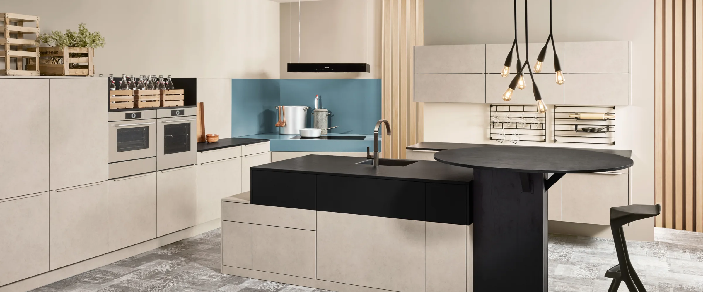 Modern kitchen showroom display with cream cabinetry, black island, blue backsplash, and stainless steel appliances.