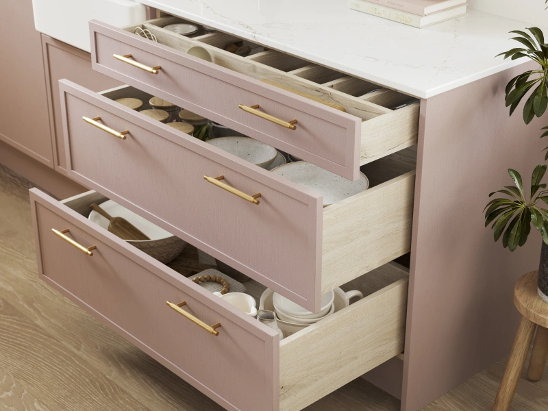 Pink kitchen cabinetry with drawers open showing organised storage and white marble countertop.