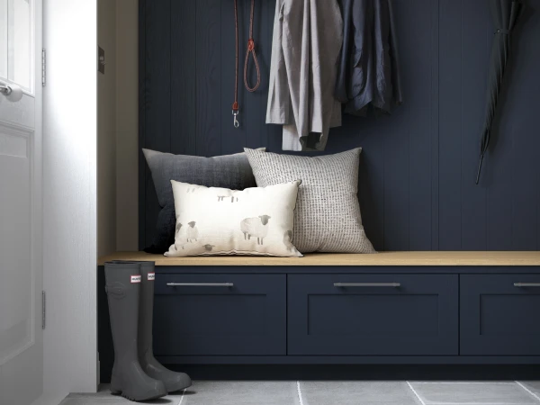 Dark navy entryway with built-in bench seating topped with cream and grey cushions and pillows, featuring wall-mounted storage for coats, hats, dog leads and umbrellas, with grey wellington boots on the floor beside the bench.
