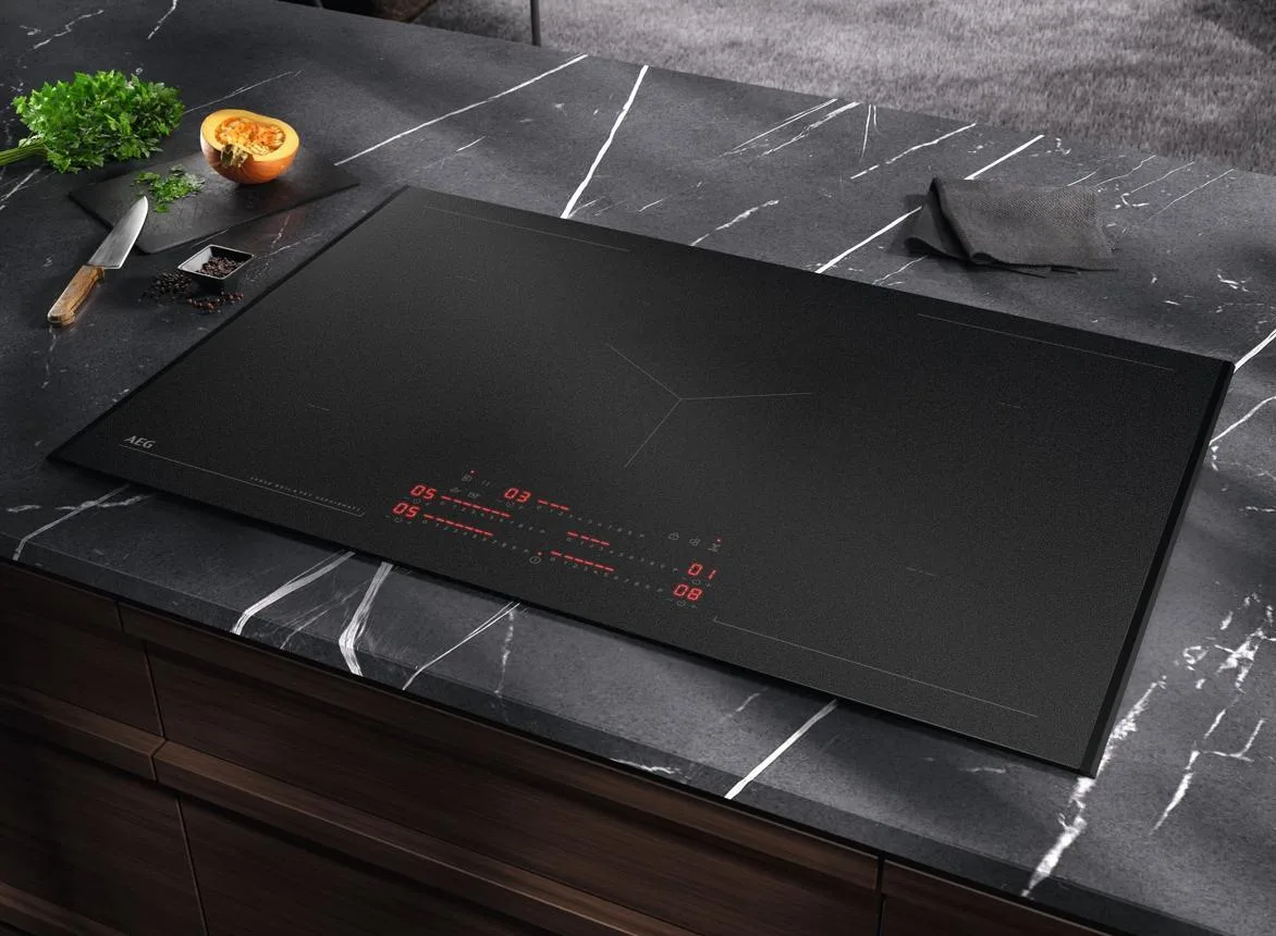 Black induction hob with red digital display built into dark marble countertop, with sliced onion and kitchen knife on cutting board to the side