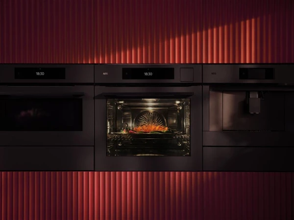 Modern kitchen with built-in black appliances and a central fireplace displaying realistic flames, flanked by vertical red ribbed panelling above and below against a dark background