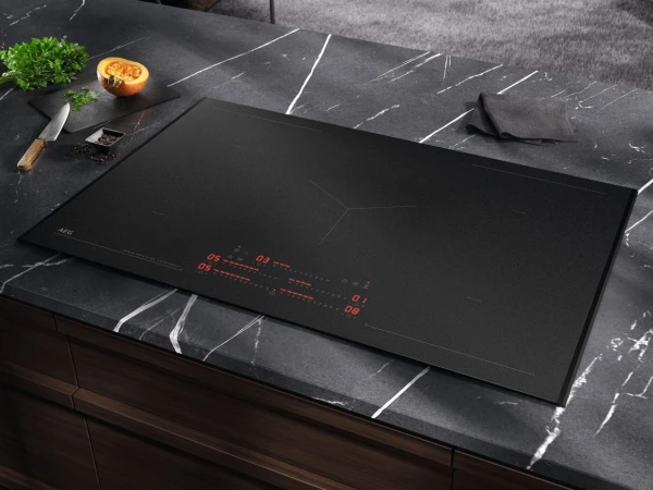 Black induction hob with red digital display built into dark marble countertop, with sliced onion and kitchen knife on cutting board to the side