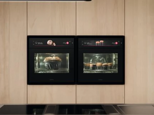 Two black built-in ovens with glass doors mounted on a light wood panel wall above a black cooktop, each displaying food inside their windows