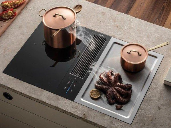 Modern induction cooktop with copper cookware and lids, featuring a pot on the left side and a saucepan on the right with pretzel-shaped pastries placed on the stovetop surface below