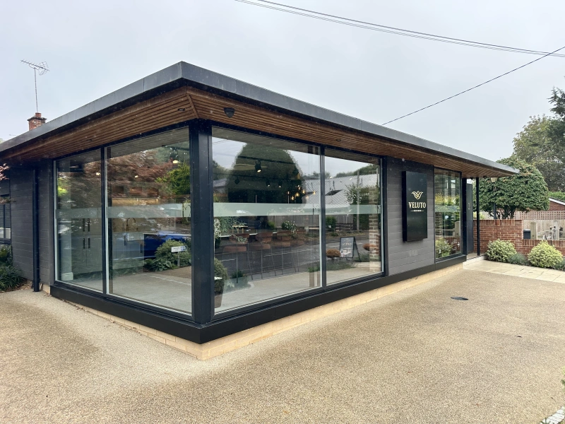 Veluto Designs showroom exterior: modern black building with large glass windows, wooden roof detail, and landscaped entrance.