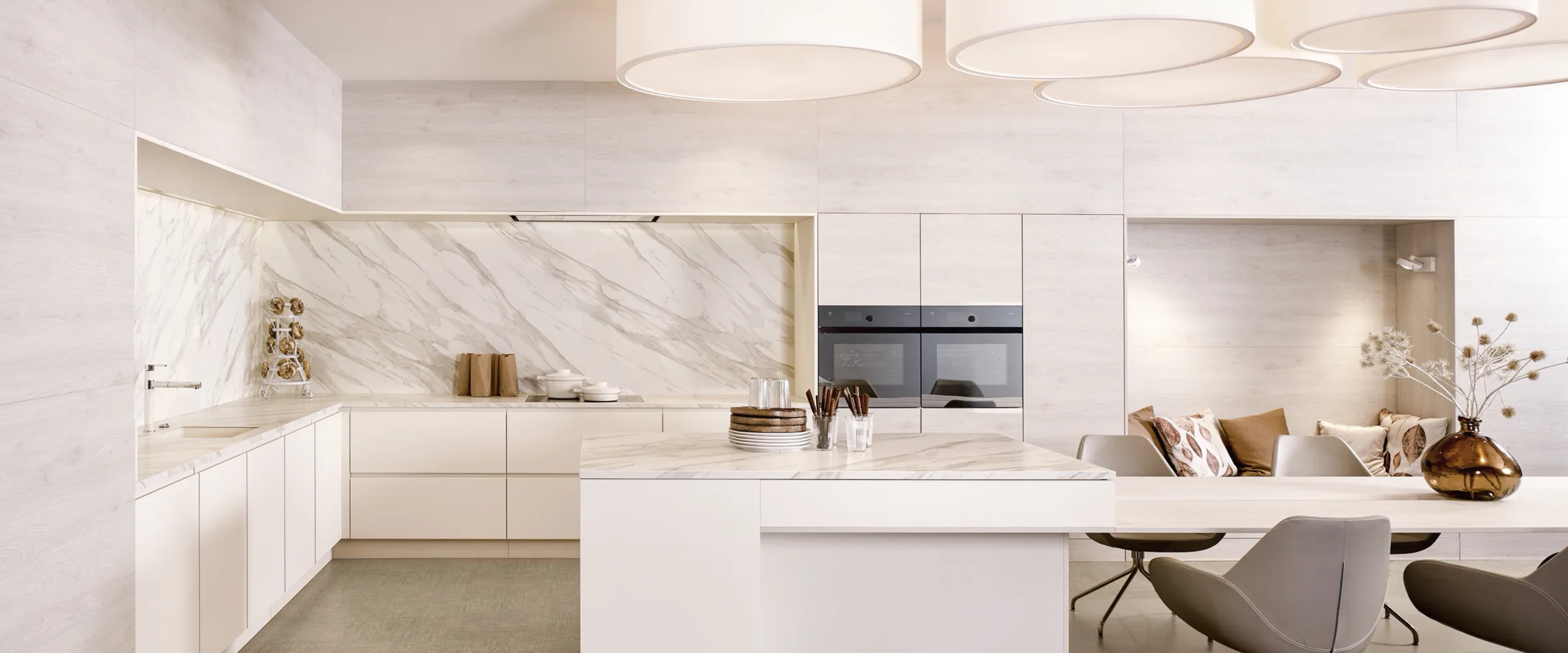 Modern white kitchen showroom with marble backsplash, island seating, and integrated appliances.
