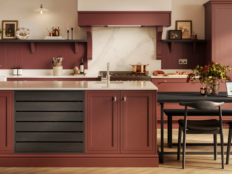 Modern kitchen with burgundy cabinetry and cream-coloured worktops, featuring a central island with black drawers and integrated dining table with two chairs, marble splashback, open shelving with decorative items, pendant lights, and stainless steel appliances.