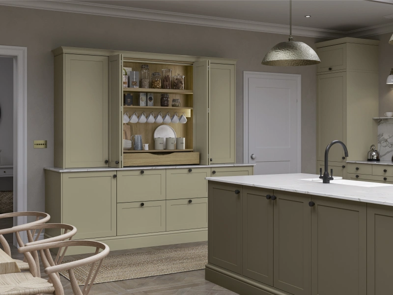Soft green kitchen with open shelving, island counter, pendant lights, and wooden chairs in foreground.