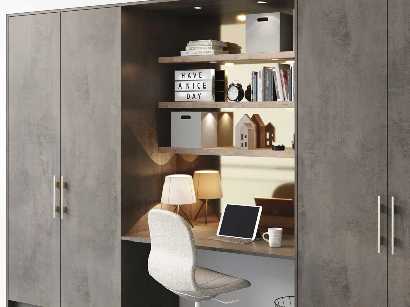 Built-in home office nook with concrete grey cabinetry, wooden shelves displaying books and decorative items, a lightbox reading "HAVE A NICE DAY", desk with tablet and lamp, and a white upholstered chair, flanked by tall storage cabinets on either side.
