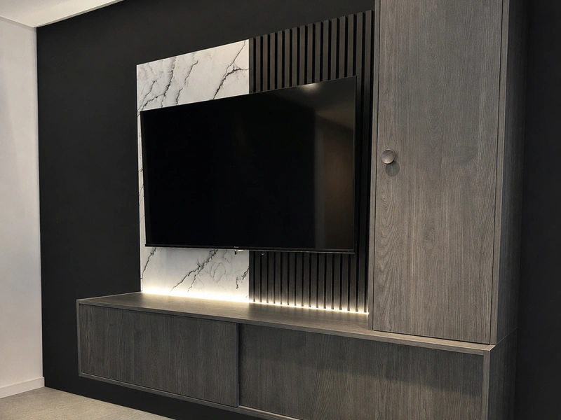 Modern media wall with flat-screen television mounted on black accent wall, featuring marble-effect panels, vertical ribbed slat detailing, grey wood-grain cabinetry below, integrated LED lighting, and a matching grey wood-grain door on the right side.