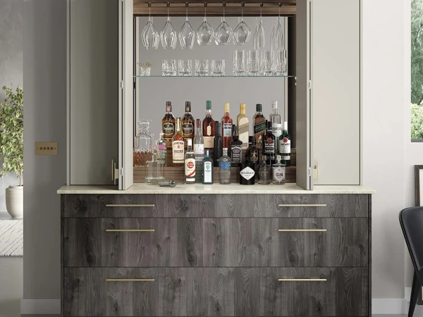 Modern home bar cabinet with dark wood base and glass-fronted upper shelving displaying various spirits bottles, decanters, and hanging wine glasses with wood trim accents