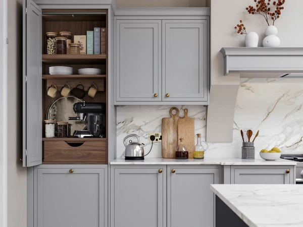 Modern kitchen with grey cabinetry and marble countertops, featuring an open shelving unit displaying kitchenware, cookbooks, bowls and hanging pans, adjacent to closed upper cabinets with brass handles, a stovetop with kettle, wooden chopping boards, and decorative white vases with dried flowers on the counter and upper shelf.