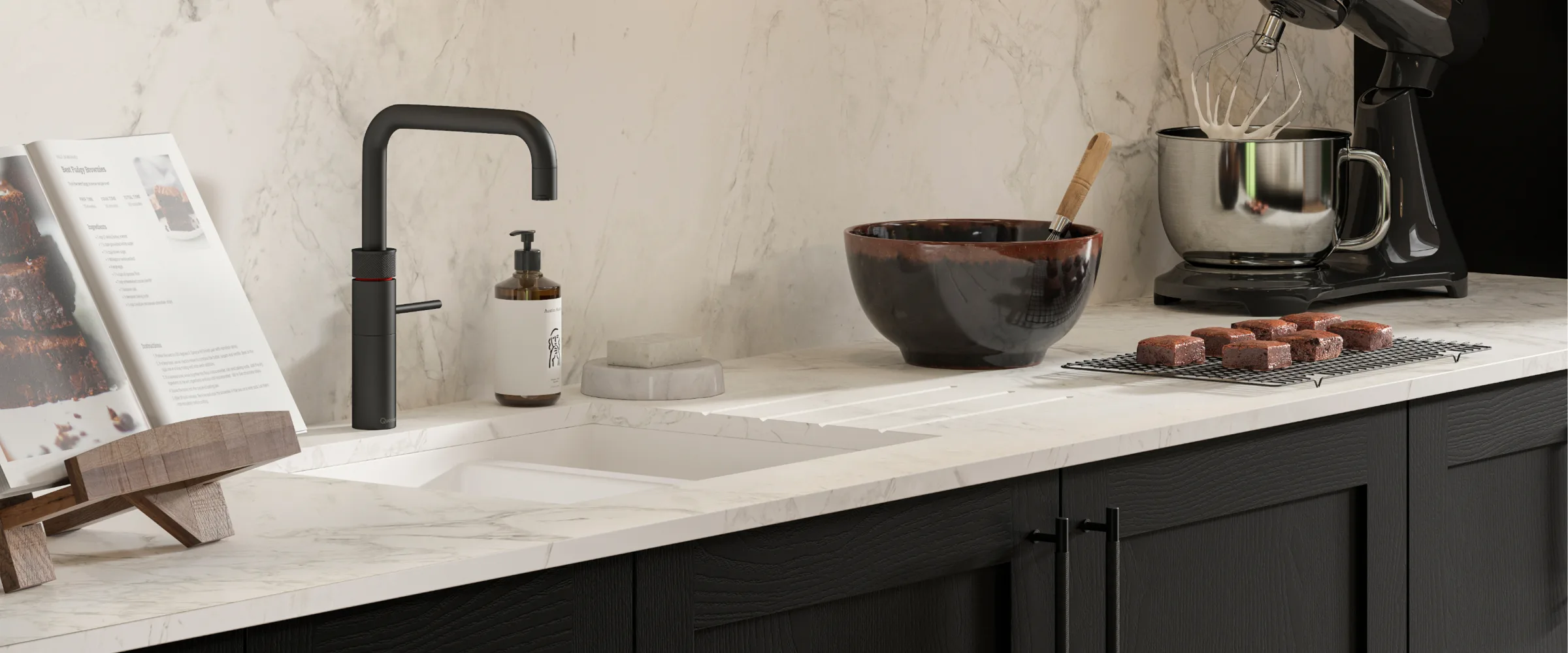 Modern kitchen countertop with marble surface and dark cabinetry, featuring a black faucet, ceramic bowl with wooden spoon, stainless steel containers, a coffee maker, freshly baked brownies on a cooling rack, recipe card holder, soap dispenser, and kitchen accessories arranged on the counter.